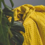 Warm yellow textured blanket draped artistically next to lush green plant indoors.