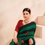 A woman in a stylish green and red saree seated on stairs in Surat, India.